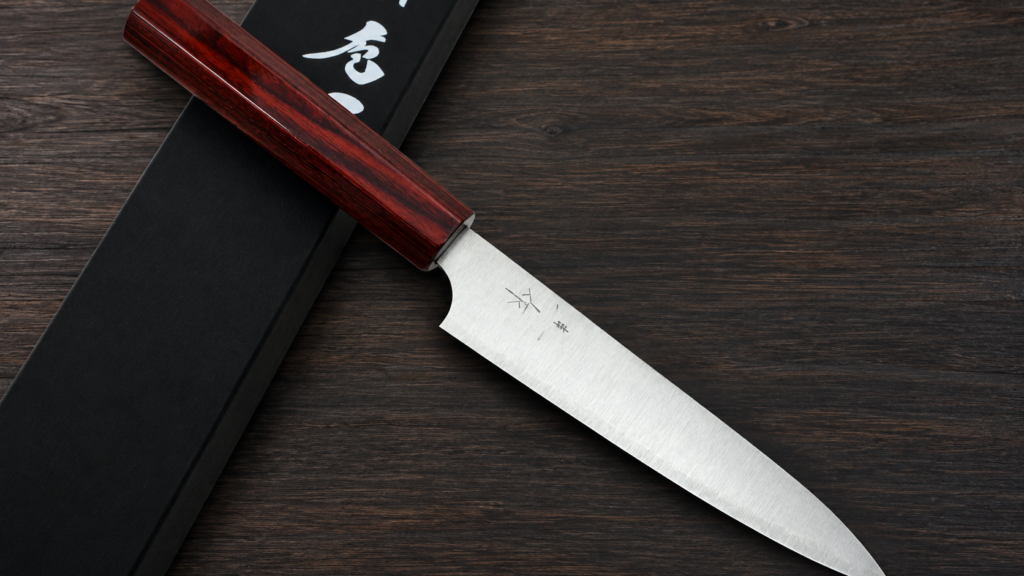Kei Kobayashi Japanese knife with a red wood handle and polished stainless steel blade displayed beside a black presentation box.