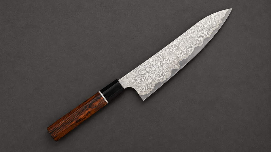 Nigara Japanese gyuto knife with an intricate Damascus-pattern blade and dark wood handle on a charcoal background.