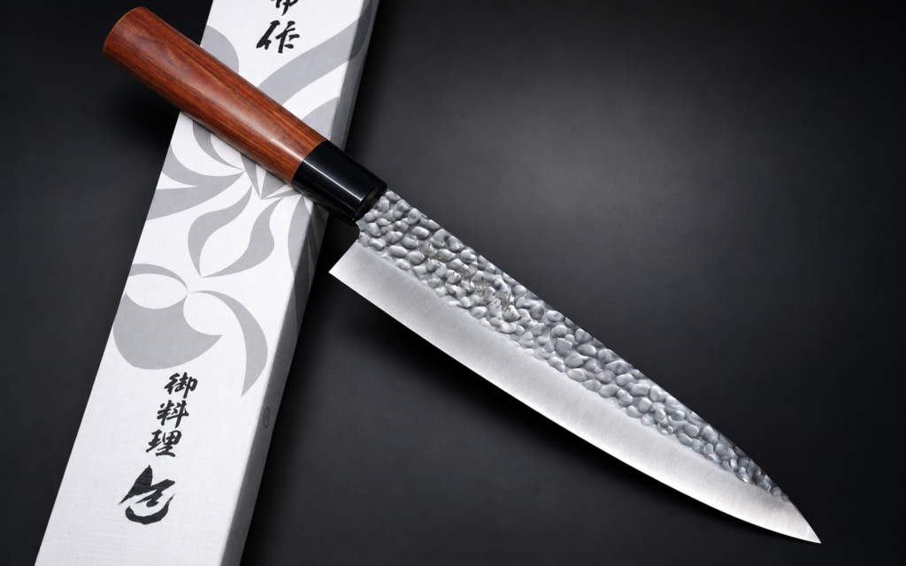Kanetsune KC-950 hammered Gyuto 210mm with a reddish-brown wooden handle resting diagonally across a white patterned presentation box on a dark background.