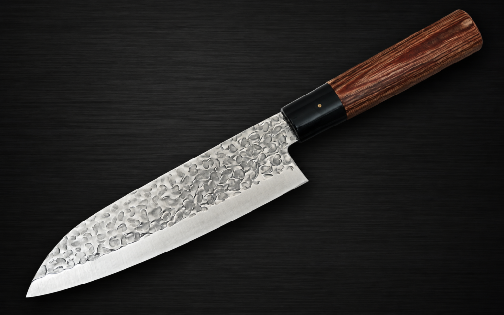Japanese santoku knife with a hammered finish and wooden handle on a dark background