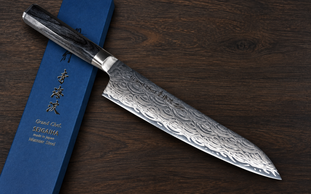 Sakai Takayuki SEIGAIHA Grand Chef Damascus Gyuto 240mm Japanese kitchen knife on a dark wooden surface with its blue presentation box.