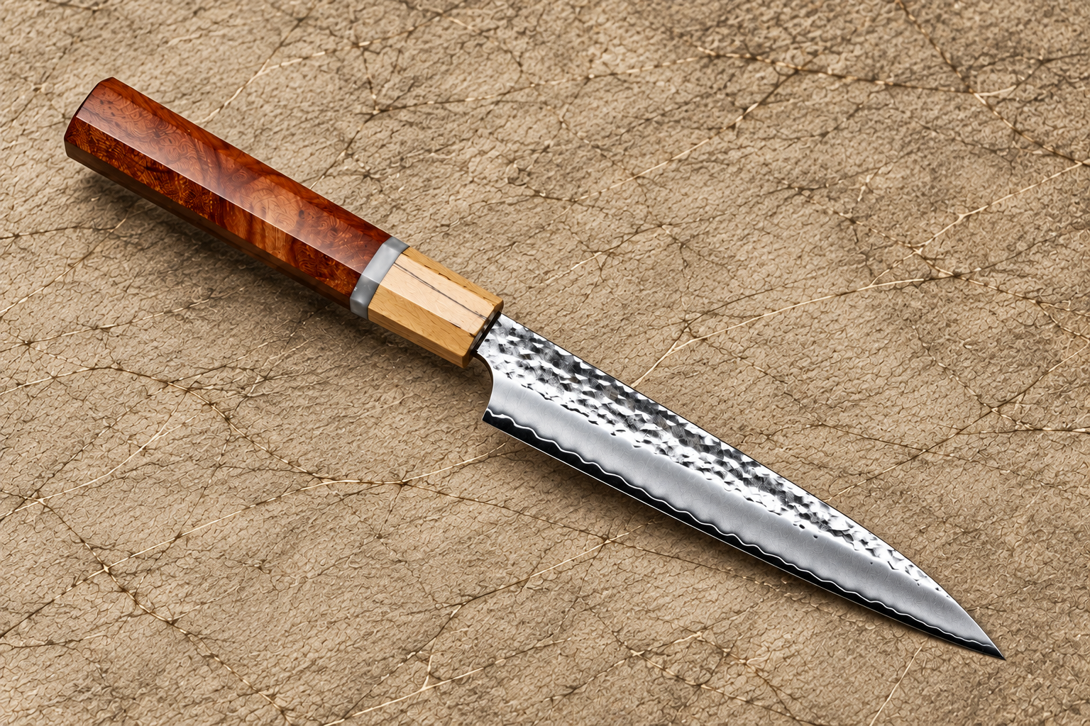 Japanese petty knife with a hammered Damascus-style blade and reddish-brown wooden handle on a textured beige background.